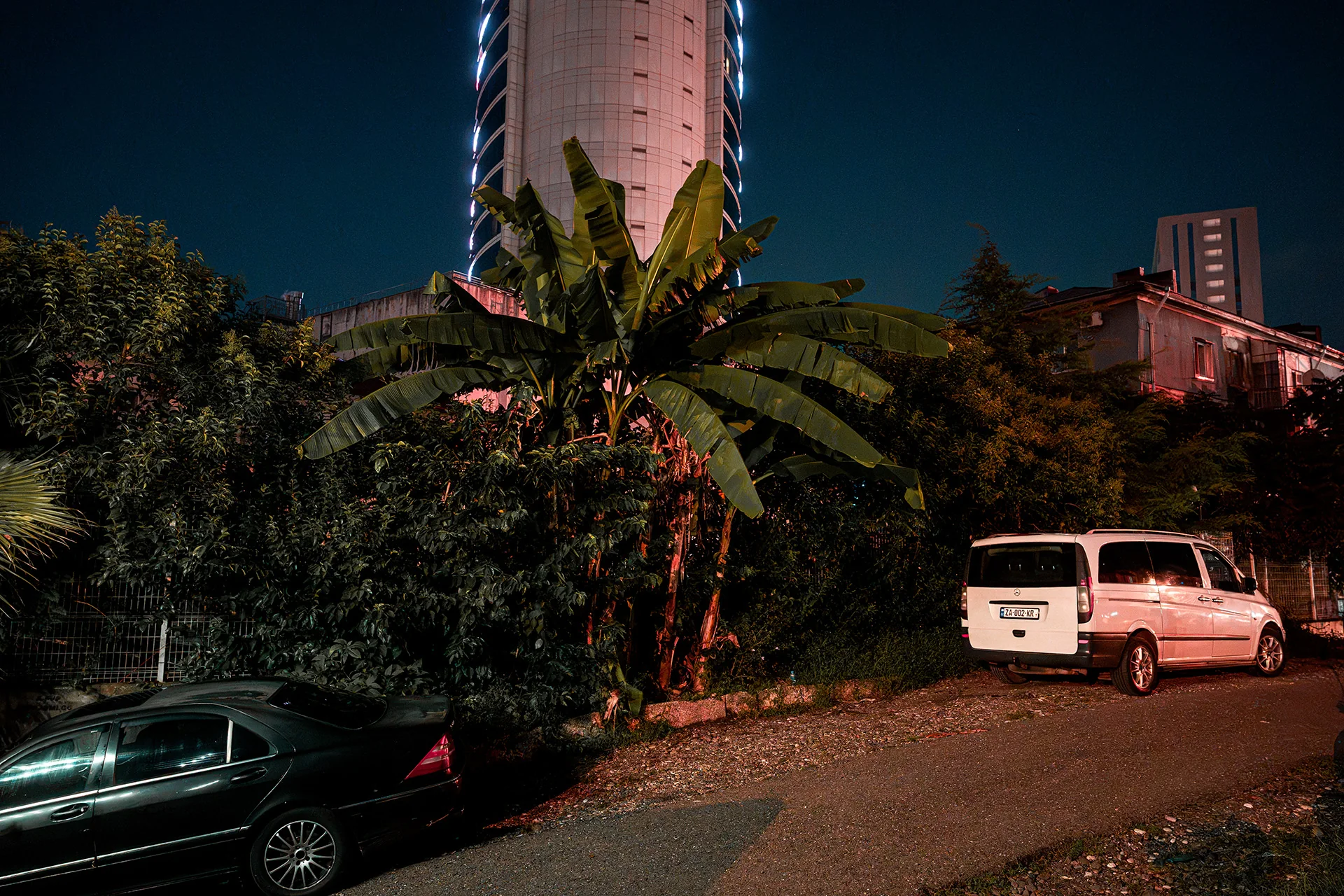 Palmy i auta nocą pod wieżowcem w Batumi