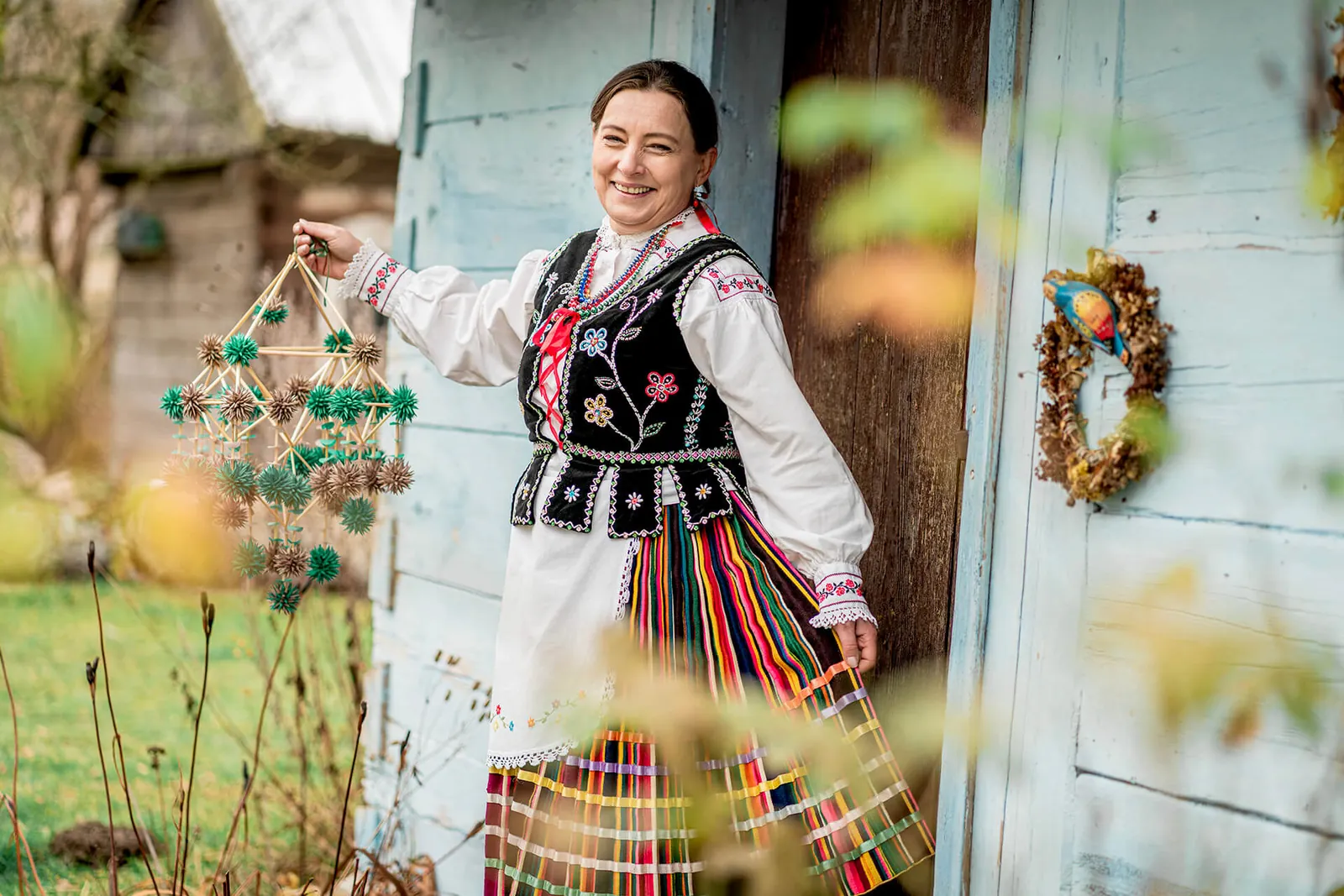 Twórczyni ludowa w stroju opoczyńskim przed niebieską ścianą chałupy, Skansen Niebowo